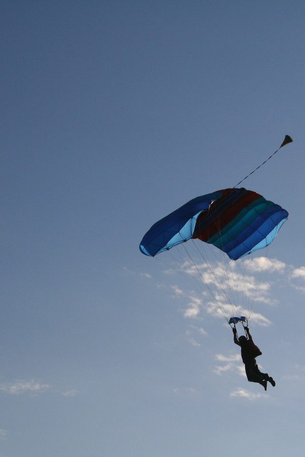 A skydiver flying a parachute through a blue sky, about to land.