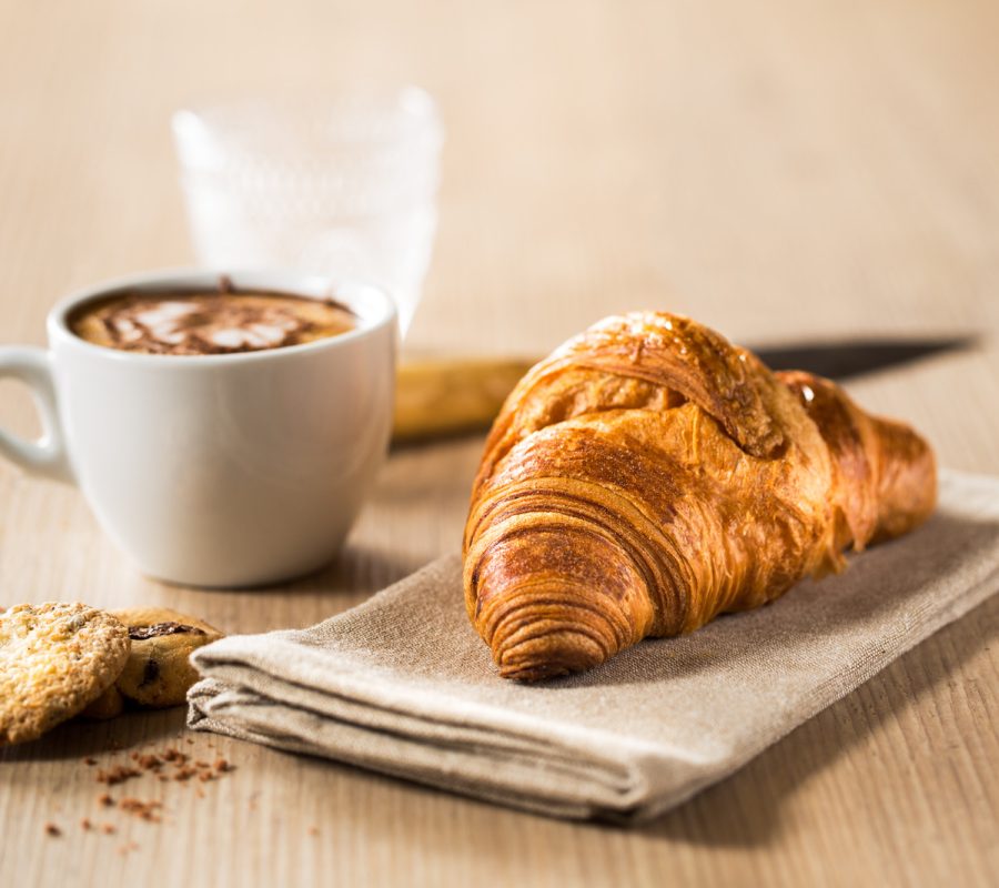 Breakfast capuccino, croissant and delicious cookies on a wooden table.